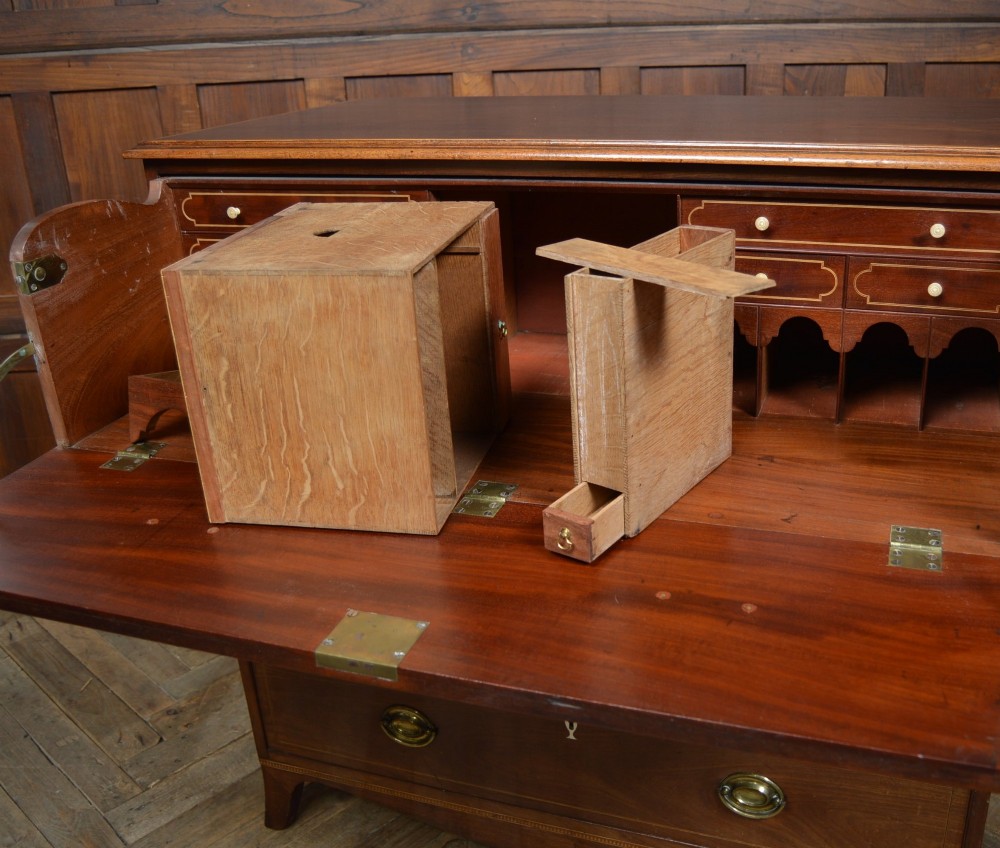 A Regency mahogany secretaire chest featuring oval inlay on the top drawer, brass oval handles, bone escutcheons, and splayed bracket feet. View V