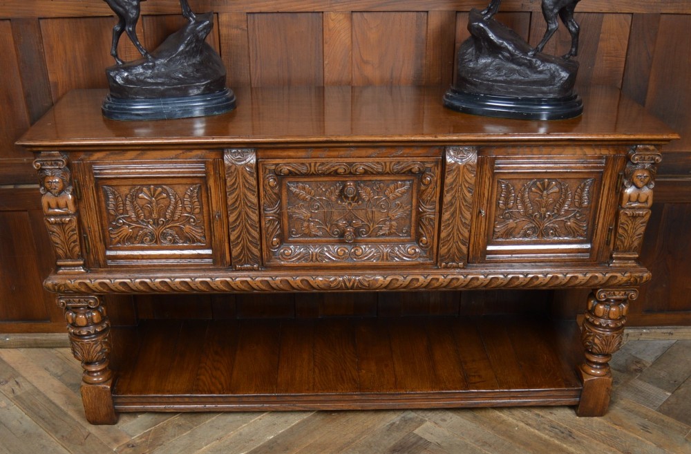 A carved dark oak Edwardian pot board dresser base featuring detailed relief carving on cupboard doors and a wide lower open shelf. View II