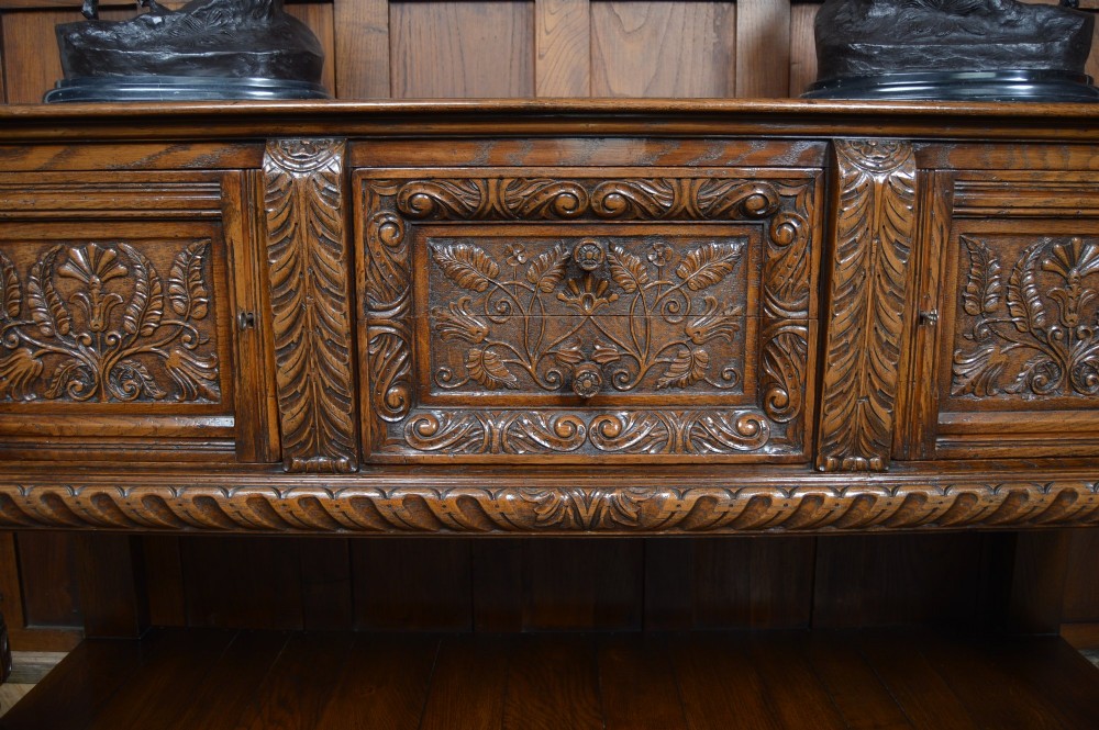 A carved dark oak Edwardian pot board dresser base featuring detailed relief carving on cupboard doors and a wide lower open shelf. View V