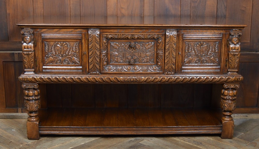 A carved dark oak Edwardian pot board dresser base featuring detailed relief carving on cupboard doors and a wide lower open shelf. View X