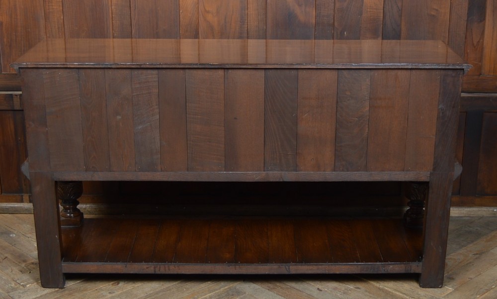 A carved dark oak Edwardian pot board dresser base featuring detailed relief carving on cupboard doors and a wide lower open shelf. View XII
