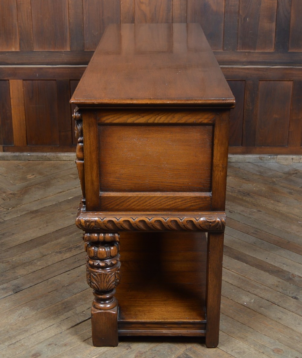 A carved dark oak Edwardian pot board dresser base featuring detailed relief carving on cupboard doors and a wide lower open shelf. View XIII