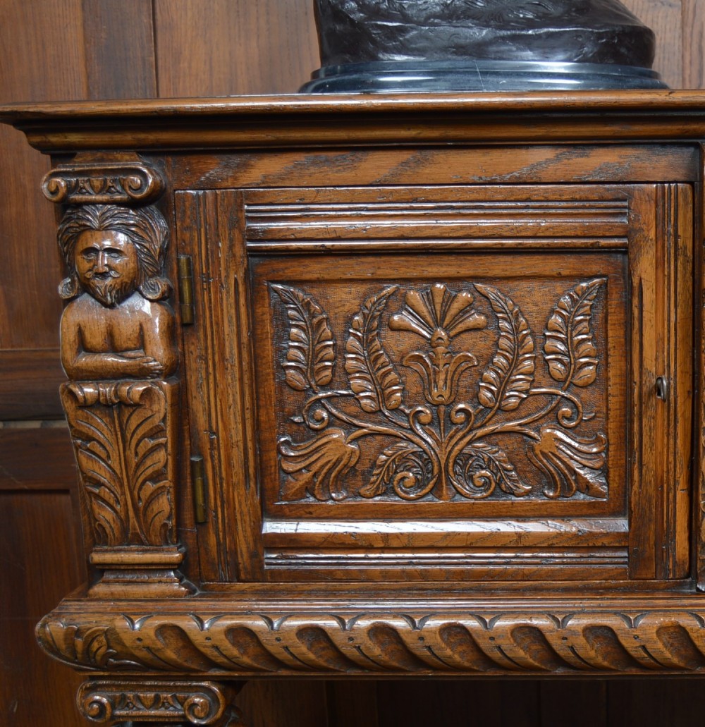 A carved dark oak Edwardian pot board dresser base featuring detailed relief carving on cupboard doors and a wide lower open shelf. View XIV