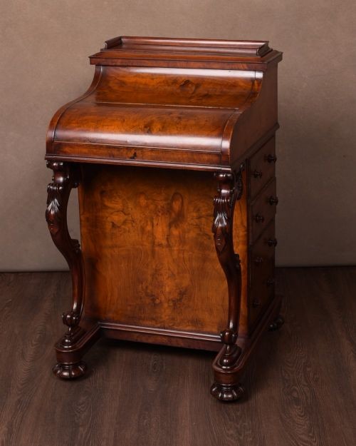 A Victorian burr walnut pop-up Davenport desk featuring carved scroll front supports, side drawers with wooden knobs, and a hinged sloping top.