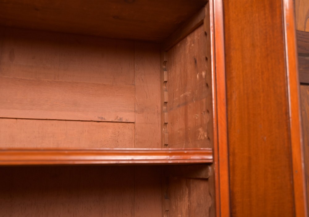 A Victorian mahogany two-part bookcase featuring a moulded cornice, two upper glazed doors with adjustable shelves, and a lower base with two arched panelled cupboard doors. View IV