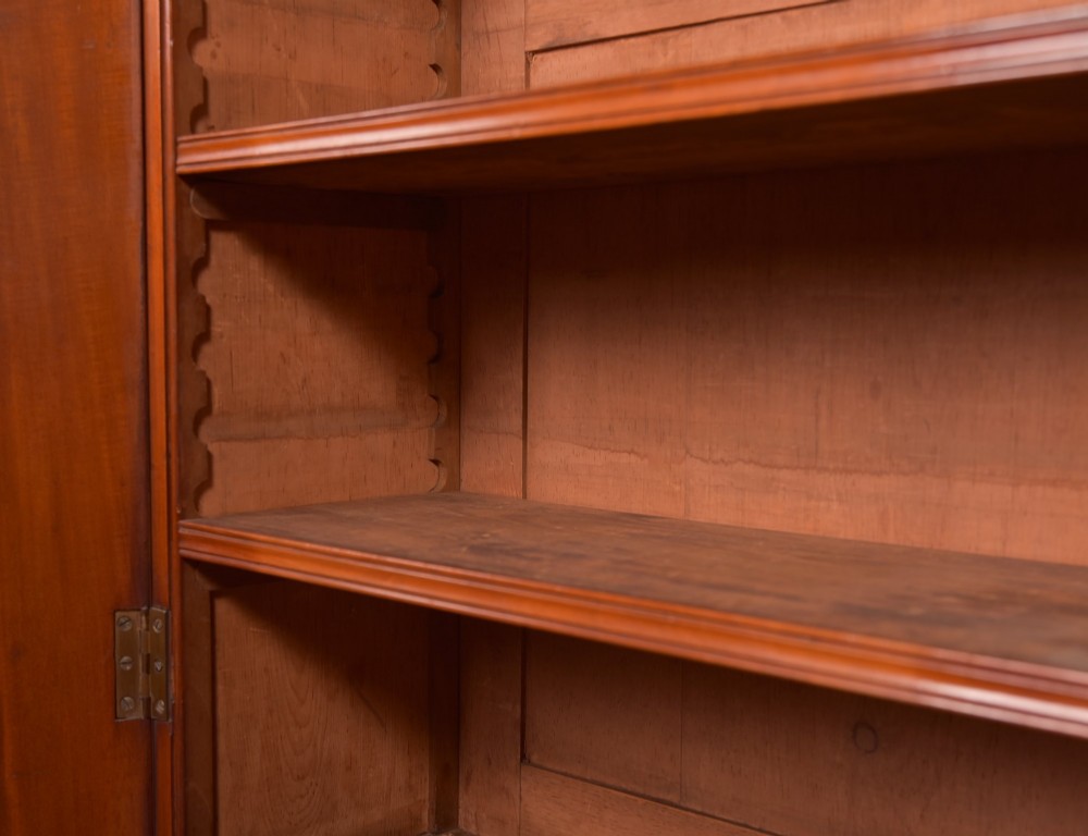 A Victorian mahogany two-part bookcase featuring a moulded cornice, two upper glazed doors with adjustable shelves, and a lower base with two arched panelled cupboard doors. View V