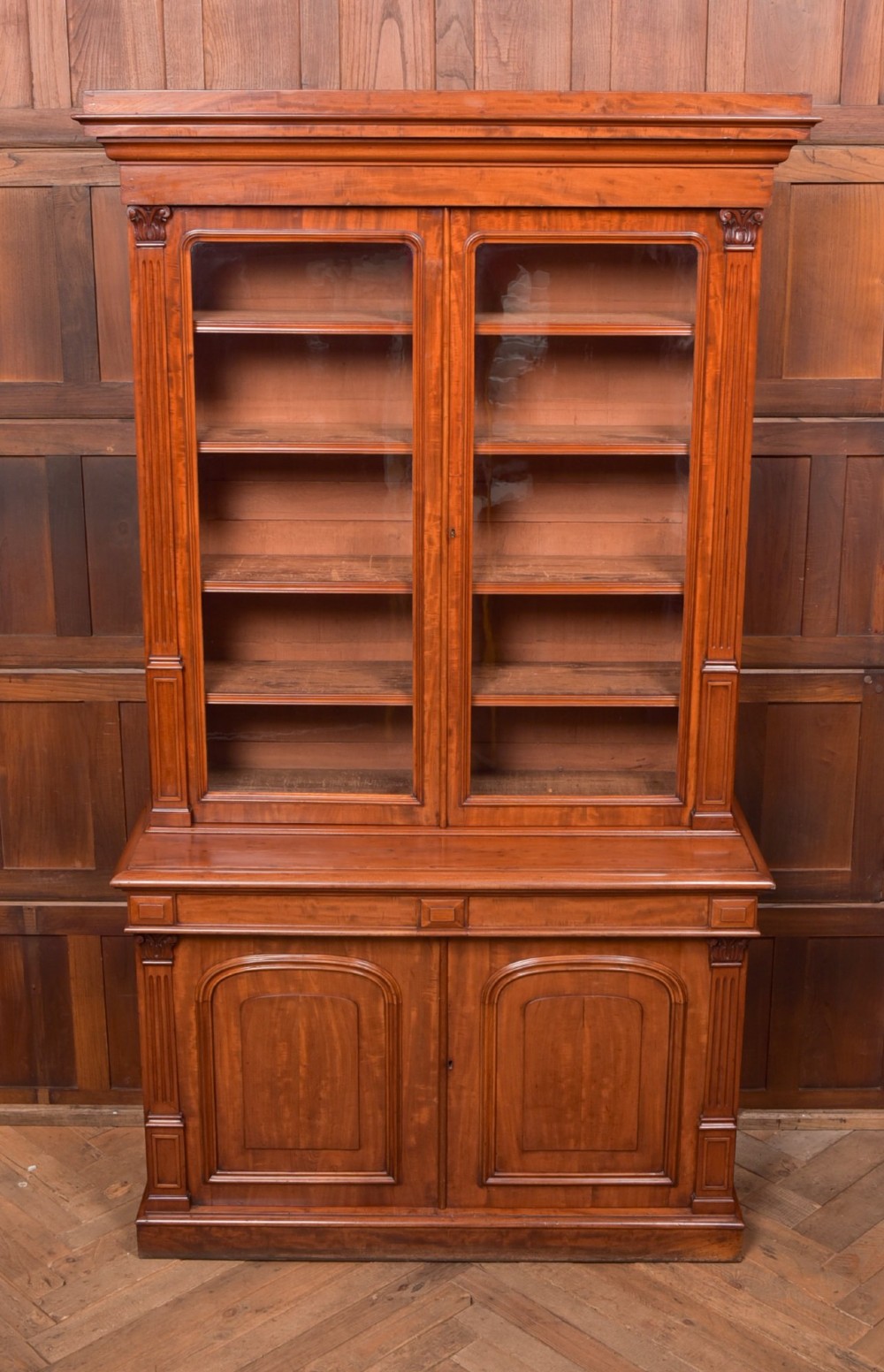 A Victorian mahogany two-part bookcase featuring a moulded cornice, two upper glazed doors with adjustable shelves, and a lower base with two arched panelled cupboard doors. View VII