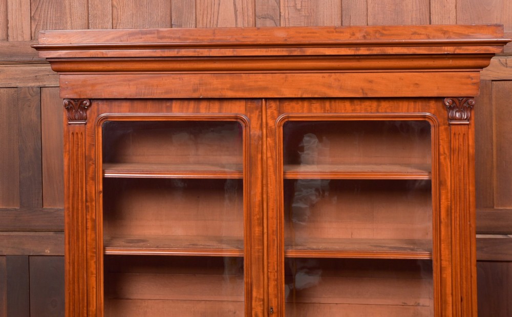 A Victorian mahogany two-part bookcase featuring a moulded cornice, two upper glazed doors with adjustable shelves, and a lower base with two arched panelled cupboard doors. View VIII