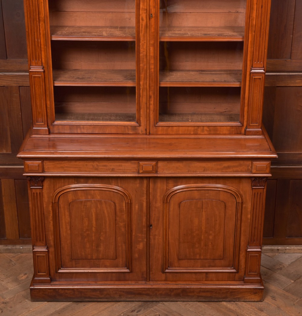 A Victorian mahogany two-part bookcase featuring a moulded cornice, two upper glazed doors with adjustable shelves, and a lower base with two arched panelled cupboard doors. View IX