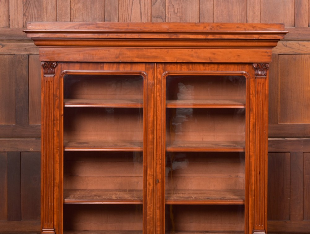 A Victorian mahogany two-part bookcase featuring a moulded cornice, two upper glazed doors with adjustable shelves, and a lower base with two arched panelled cupboard doors. View X