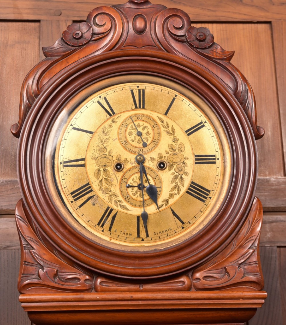 A Victorian Scottish mahogany drumhead longcase clock featuring a circular hood with carved scrollwork, a brass dial, and a flame mahogany trunk. View II