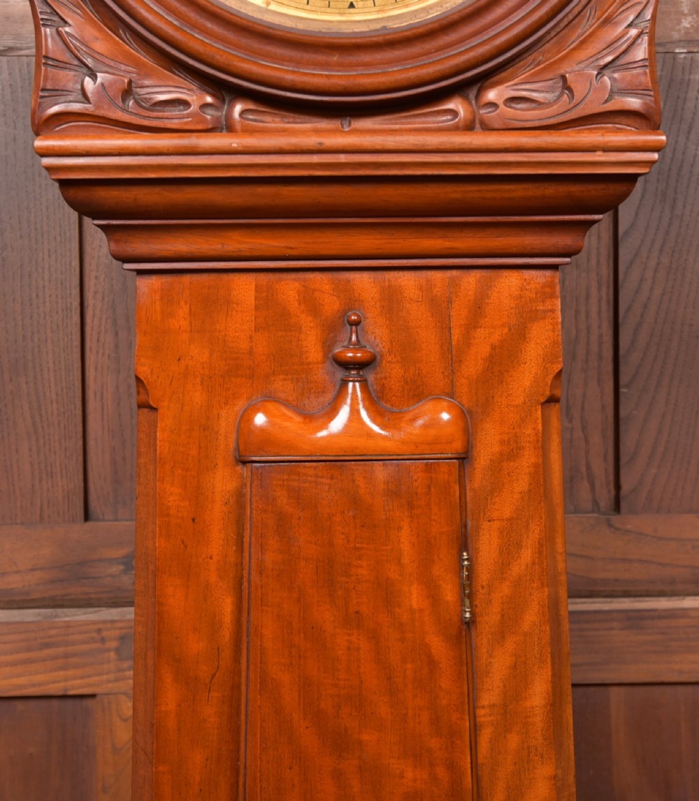 A Victorian Scottish mahogany drumhead longcase clock featuring a circular hood with carved scrollwork, a brass dial, and a flame mahogany trunk. View III