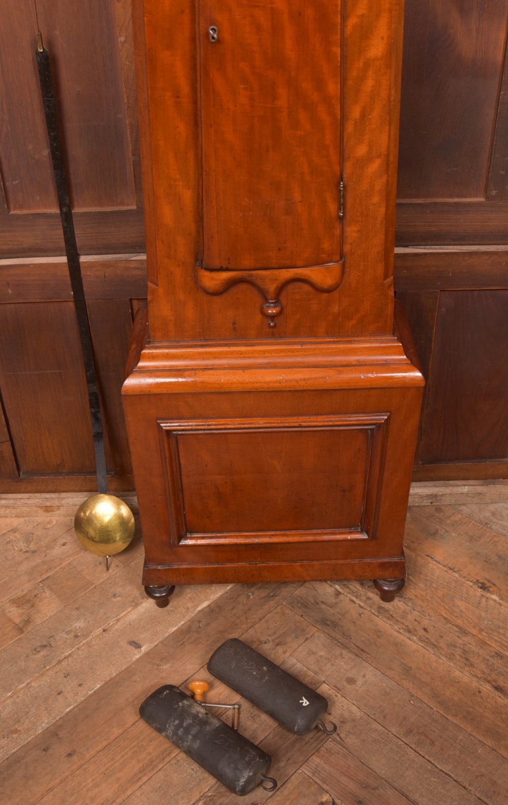 A Victorian Scottish mahogany drumhead longcase clock featuring a circular hood with carved scrollwork, a brass dial, and a flame mahogany trunk. View IV