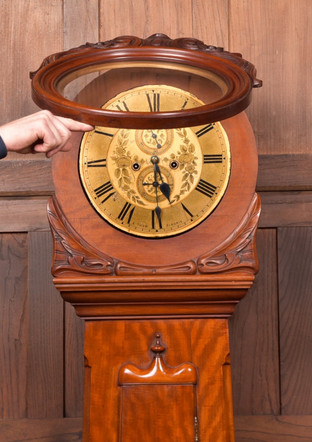 A Victorian Scottish mahogany drumhead longcase clock featuring a circular hood with carved scrollwork, a brass dial, and a flame mahogany trunk. View VIII