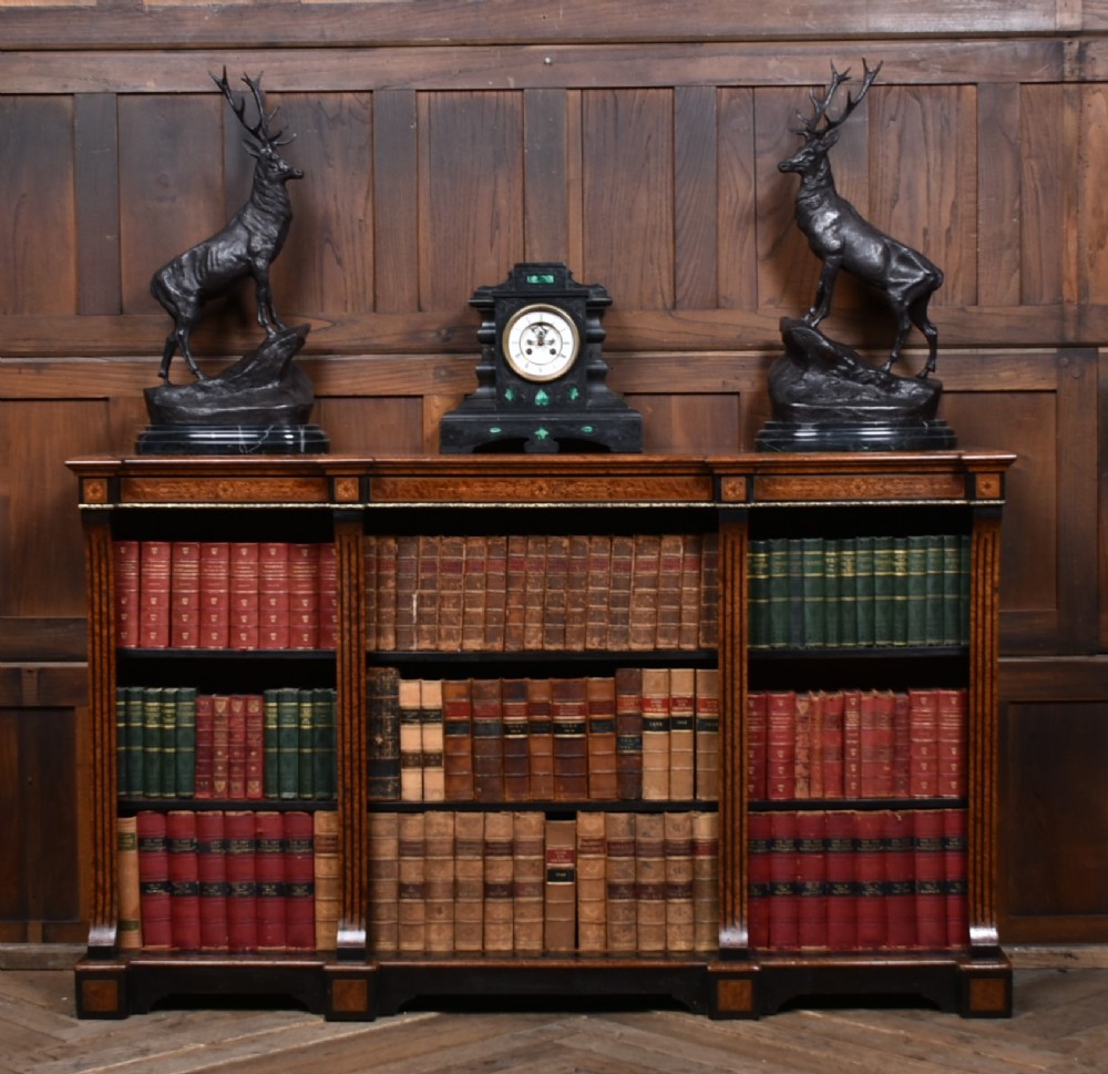 A low Victorian open bookcase featuring three sections of open shelving, rich amboyna wood veneer, ebonised borders, and delicate marquetry inlays.