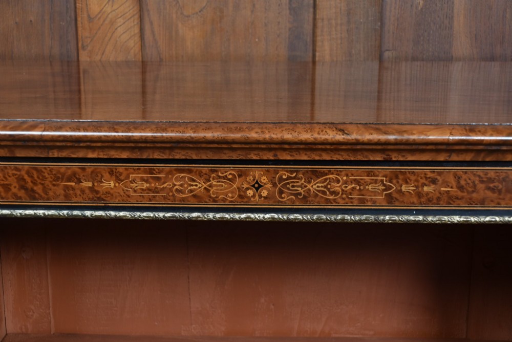 A low Victorian open bookcase featuring three sections of open shelving, rich amboyna wood veneer, ebonised borders, and delicate marquetry inlays. View V