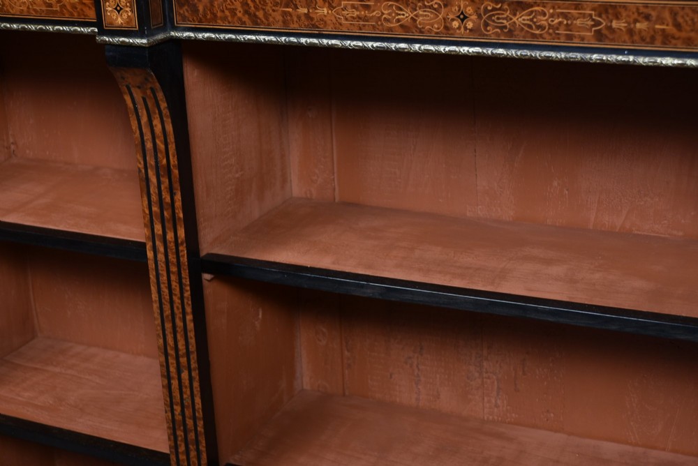 A low Victorian open bookcase featuring three sections of open shelving, rich amboyna wood veneer, ebonised borders, and delicate marquetry inlays. View VI