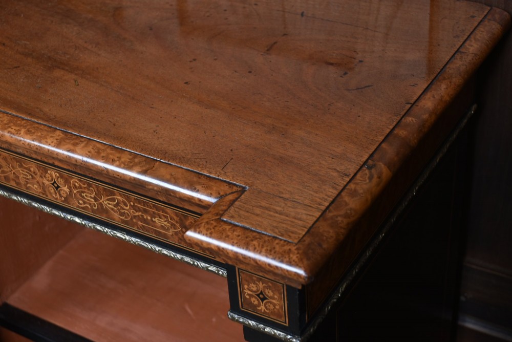 A low Victorian open bookcase featuring three sections of open shelving, rich amboyna wood veneer, ebonised borders, and delicate marquetry inlays. View X