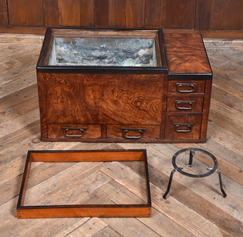 A traditional Japanese wooden hibachi brazier featuring rich figured wood grain, a copper-lined inner well, multiple small drawers, and iron bail handles. View VI