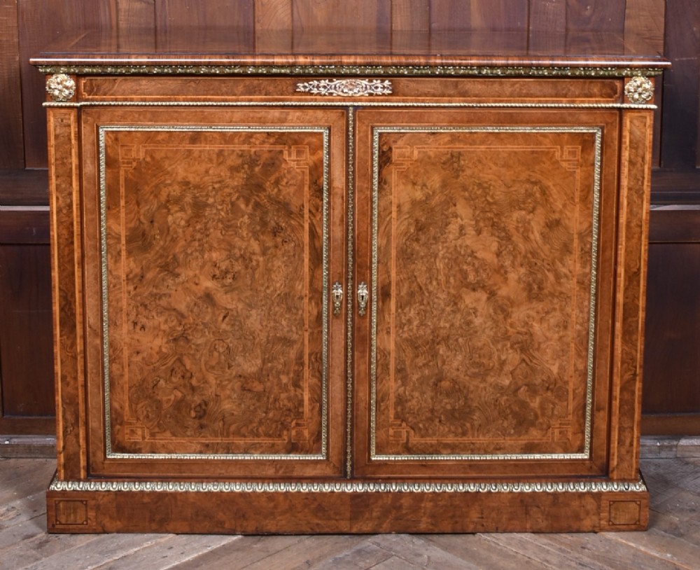 A 19th-century Victorian burr walnut side cabinet featuring two panelled doors with decorative brass mounts and a plinth base.