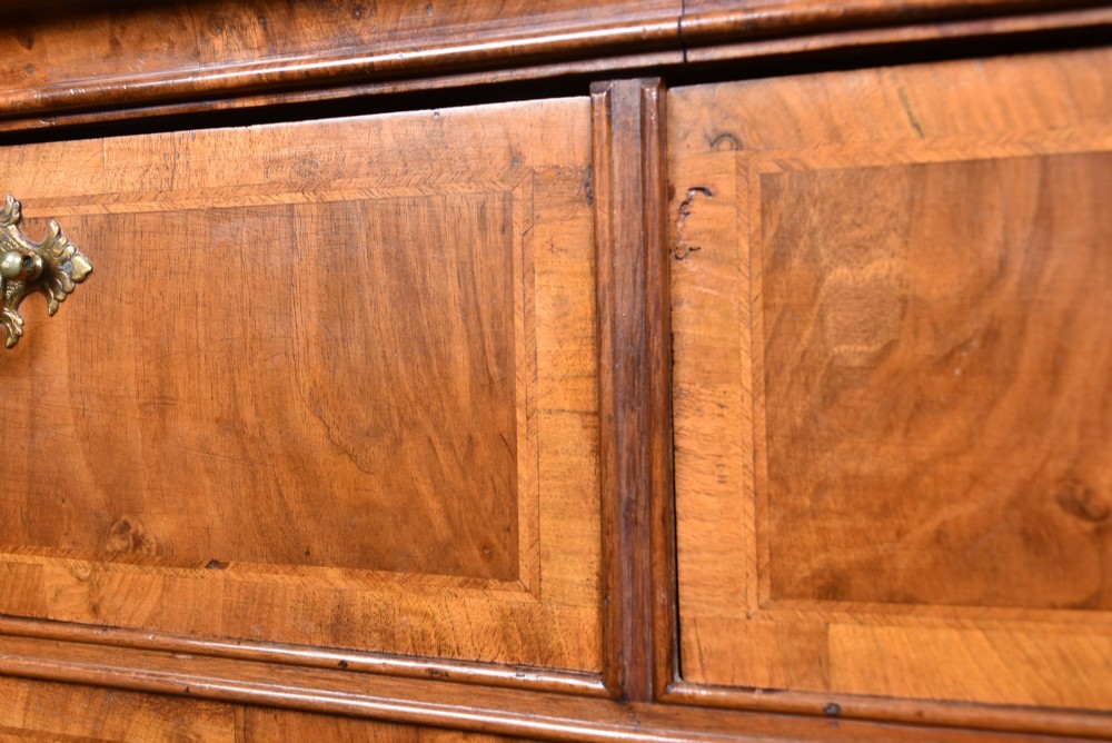 An eighteenth-century figured walnut chest on stand featuring brass hardware, crossbanded drawers, an arched apron, and cabriole legs. View V