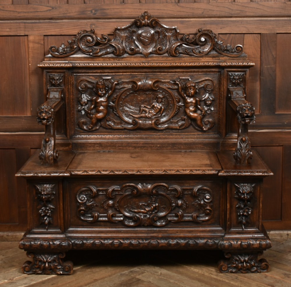 A heavily carved 19th-century Italian walnut cassapanca bench featuring relief panels of cherubs, scrolled cresting, and carved lion armrests.