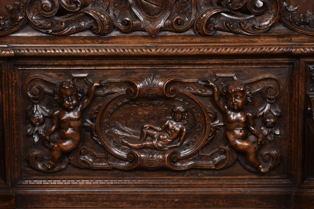 A heavily carved 19th-century Italian walnut cassapanca bench featuring relief panels of cherubs, scrolled cresting, and carved lion armrests. View II