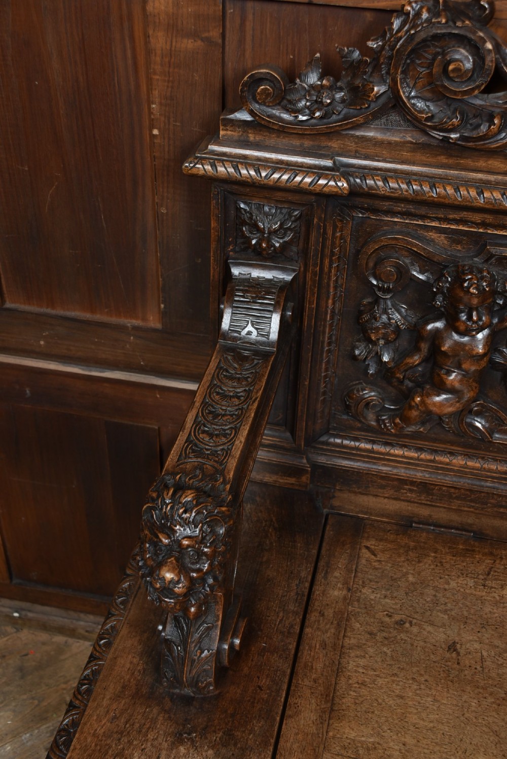 A heavily carved 19th-century Italian walnut cassapanca bench featuring relief panels of cherubs, scrolled cresting, and carved lion armrests. View IV