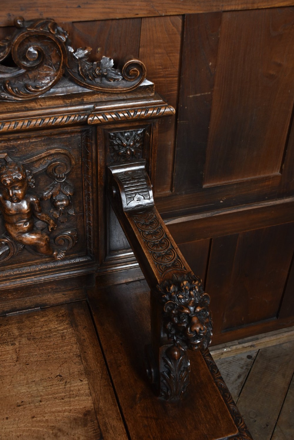 A heavily carved 19th-century Italian walnut cassapanca bench featuring relief panels of cherubs, scrolled cresting, and carved lion armrests. View V