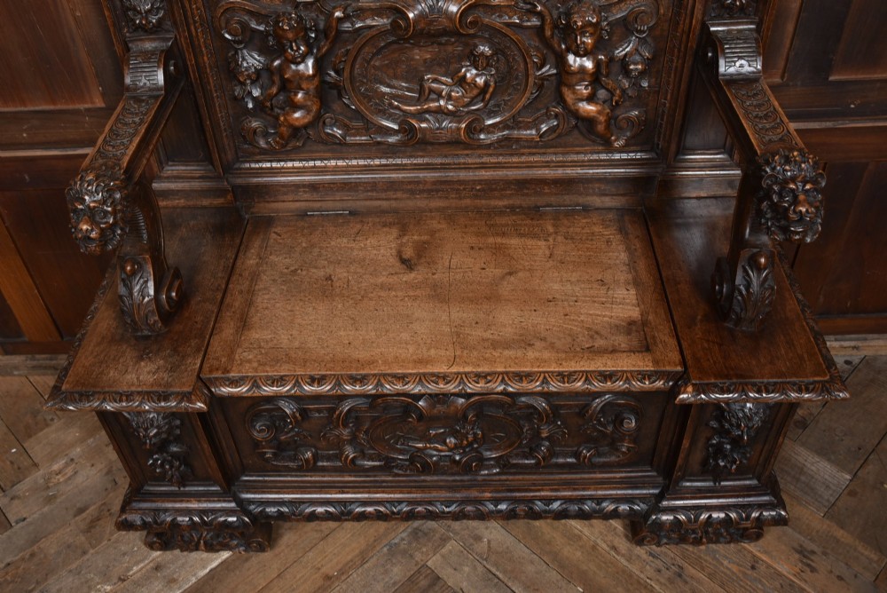 A heavily carved 19th-century Italian walnut cassapanca bench featuring relief panels of cherubs, scrolled cresting, and carved lion armrests. View VI