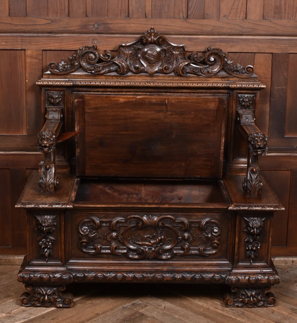 A heavily carved 19th-century Italian walnut cassapanca bench featuring relief panels of cherubs, scrolled cresting, and carved lion armrests. View VII