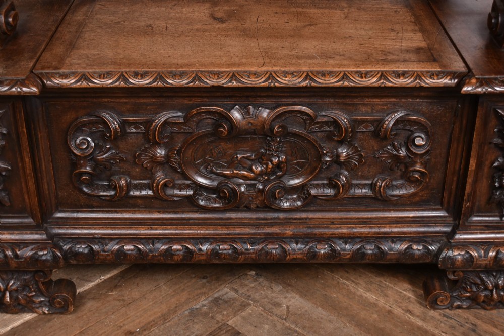A heavily carved 19th-century Italian walnut cassapanca bench featuring relief panels of cherubs, scrolled cresting, and carved lion armrests. View VIII