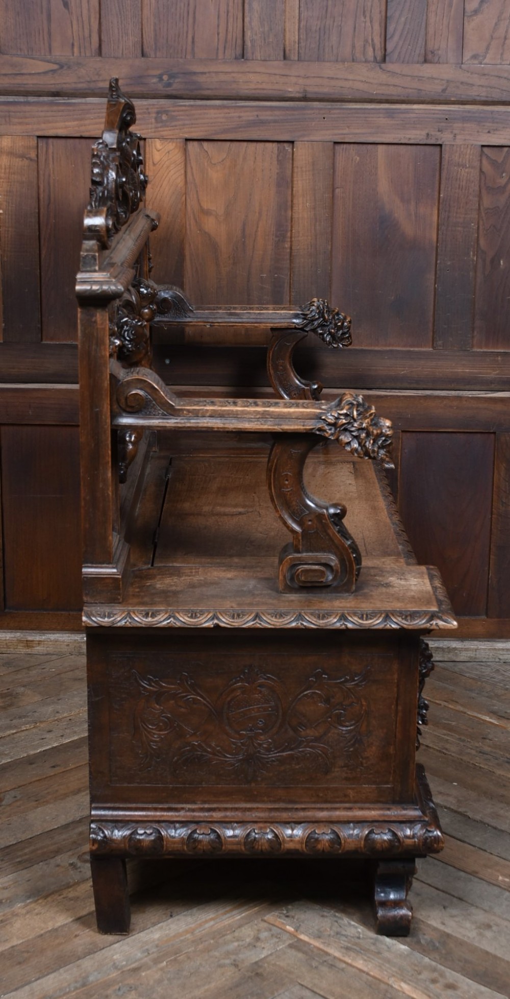 A heavily carved 19th-century Italian walnut cassapanca bench featuring relief panels of cherubs, scrolled cresting, and carved lion armrests. View XI