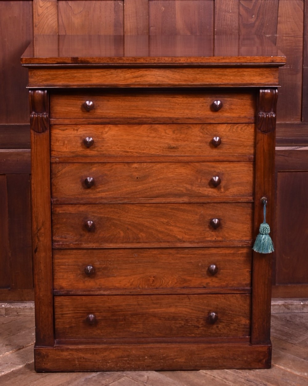 A tall Victorian rosewood Wellington chest featuring six graduated drawers with turned wooden knobs, carved corbels, and a right-side locking bar. View II