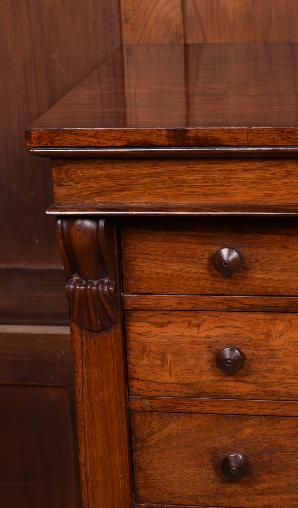 A tall Victorian rosewood Wellington chest featuring six graduated drawers with turned wooden knobs, carved corbels, and a right-side locking bar. View IV
