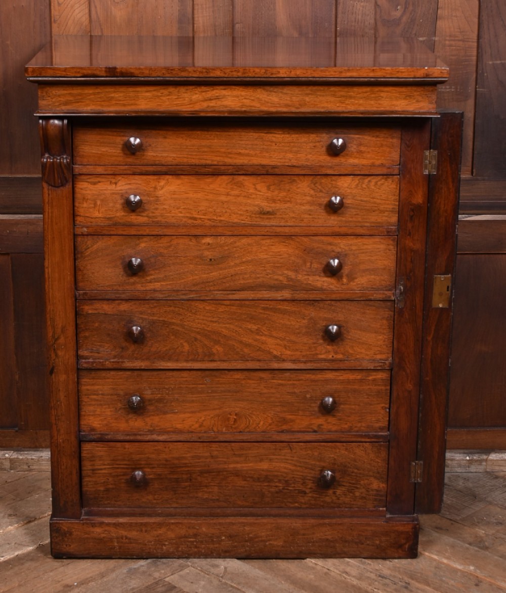 A tall Victorian rosewood Wellington chest featuring six graduated drawers with turned wooden knobs, carved corbels, and a right-side locking bar. View VI