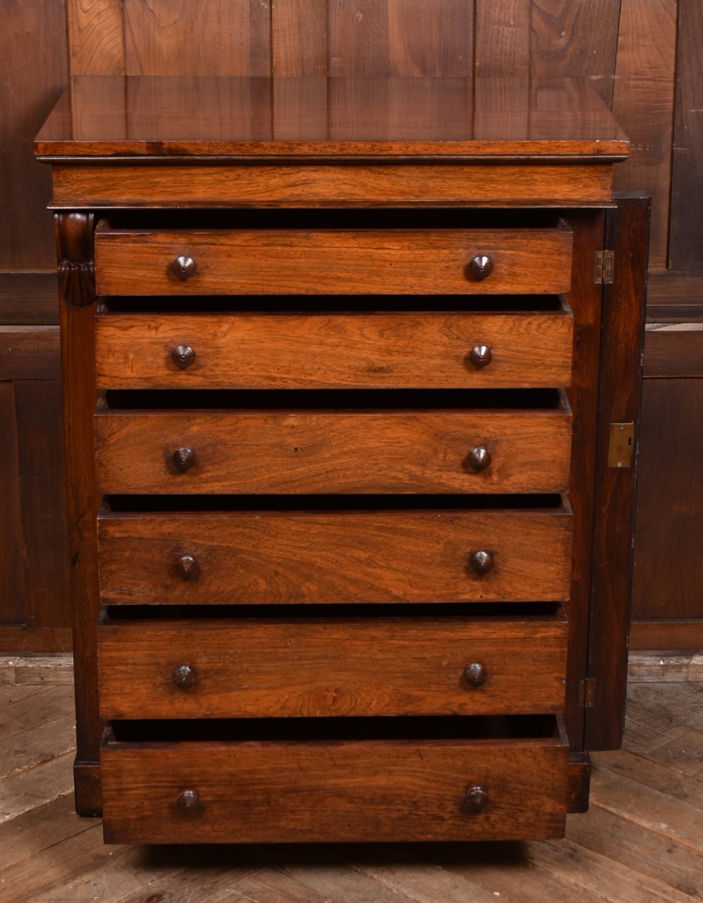 A tall Victorian rosewood Wellington chest featuring six graduated drawers with turned wooden knobs, carved corbels, and a right-side locking bar. View VII
