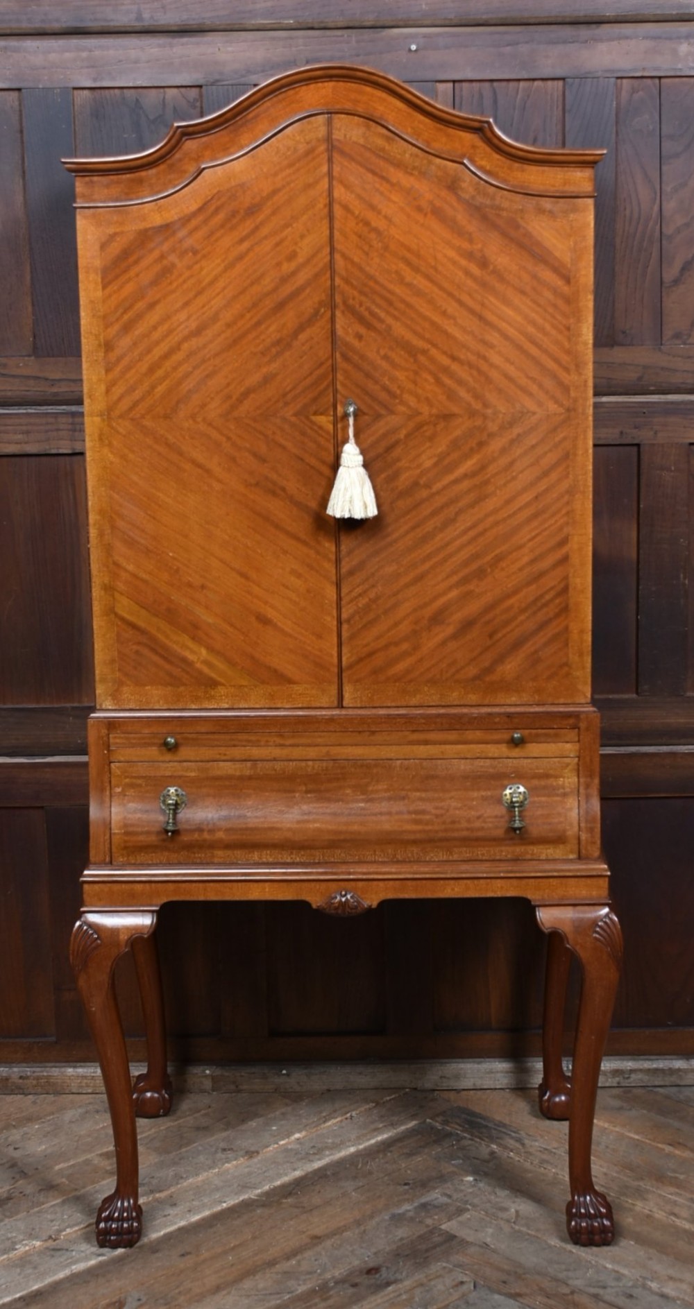 An Edwardian mahogany drinks cabinet on stand featuring chevron-matched wood veneer doors, a lower drawer with brass drop handles, and carved cabriole legs ending in ball and claw feet.