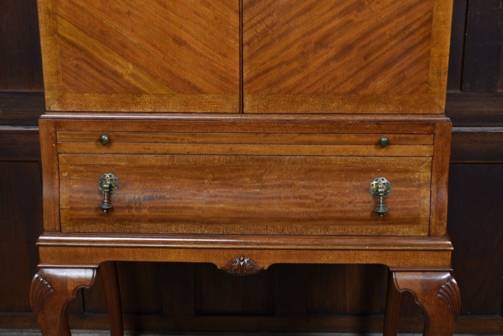 An Edwardian mahogany drinks cabinet on stand featuring chevron-matched wood veneer doors, a lower drawer with brass drop handles, and carved cabriole legs ending in ball and claw feet. View XIV