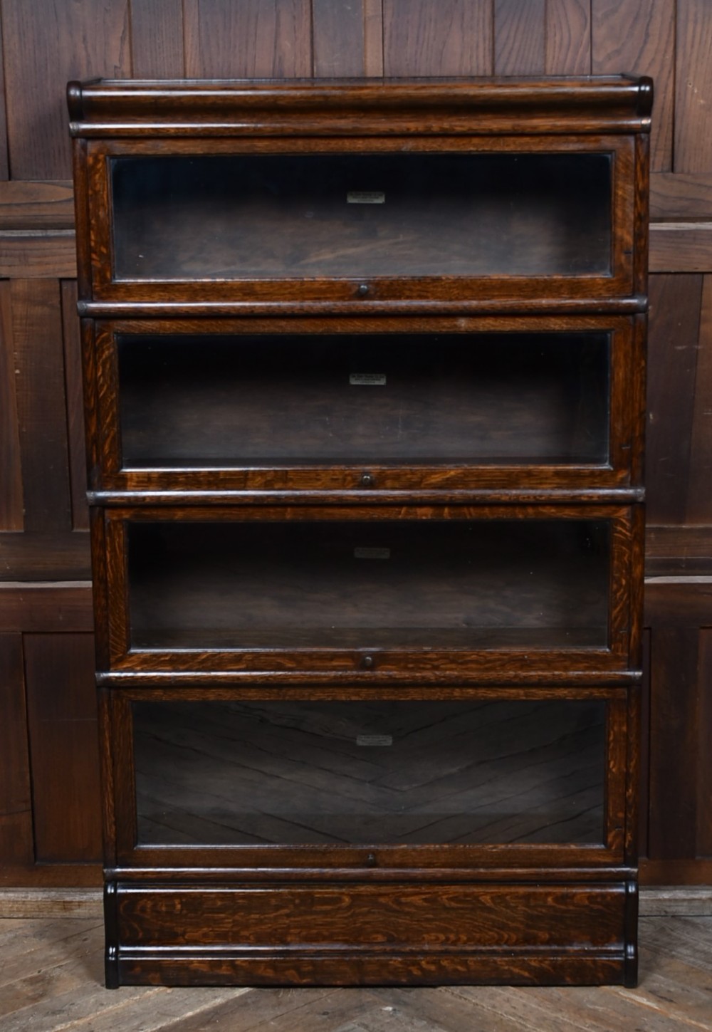 An Edwardian dark oak four-tier Globe Wernicke sectional bookcase featuring glass up-and-over doors and brass maker labels.