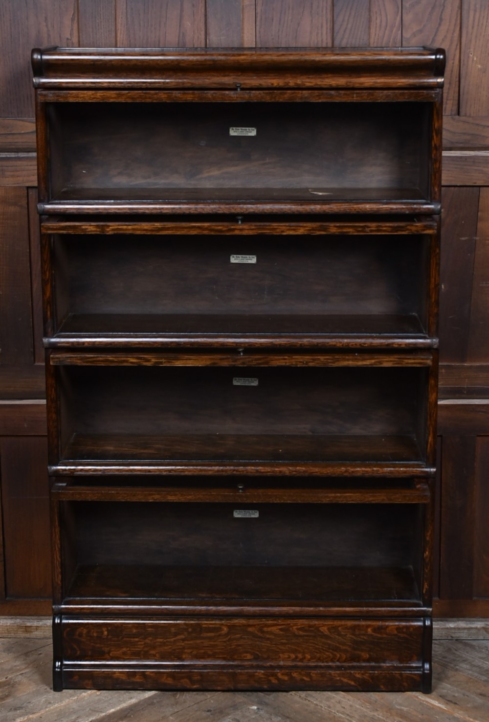 An Edwardian dark oak four-tier Globe Wernicke sectional bookcase featuring glass up-and-over doors and brass maker labels. View V