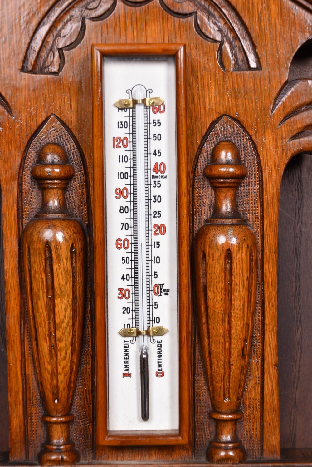 A Victorian carved oak wall barometer featuring an upper thermometer flanked by turned urn finials and a lower round aneroid dial with red and black text. View VI