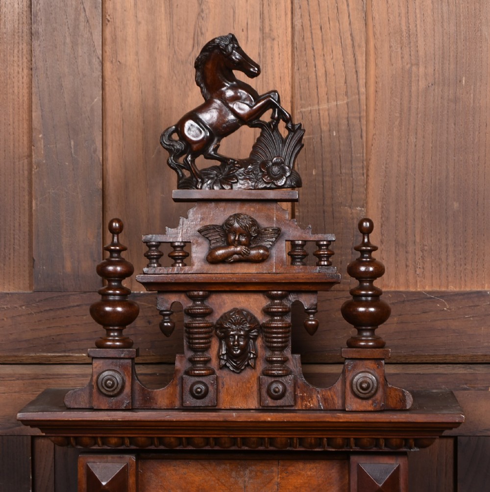 An antique dark walnut wall clock featuring a carved horse crest, turned side pilasters, and a decorative brass pendulum behind a glass door. View II