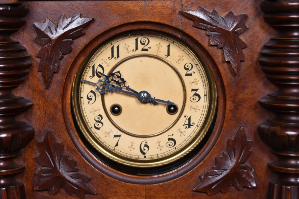 An antique dark walnut wall clock featuring a carved horse crest, turned side pilasters, and a decorative brass pendulum behind a glass door. View III