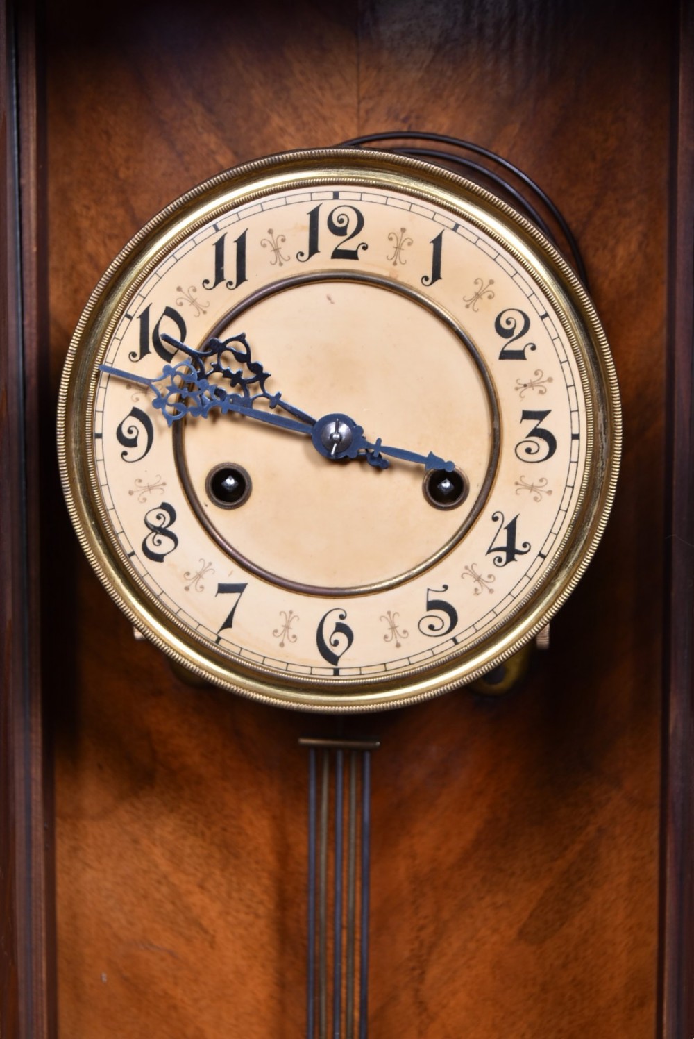 An antique dark walnut wall clock featuring a carved horse crest, turned side pilasters, and a decorative brass pendulum behind a glass door. View V