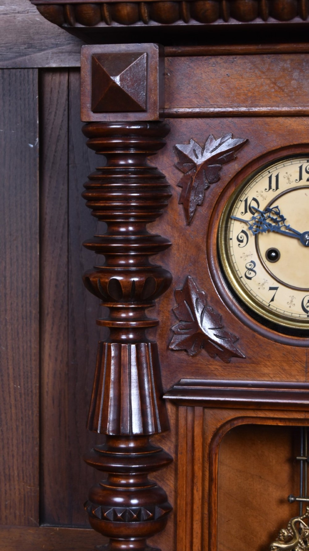 An antique dark walnut wall clock featuring a carved horse crest, turned side pilasters, and a decorative brass pendulum behind a glass door. View VIII