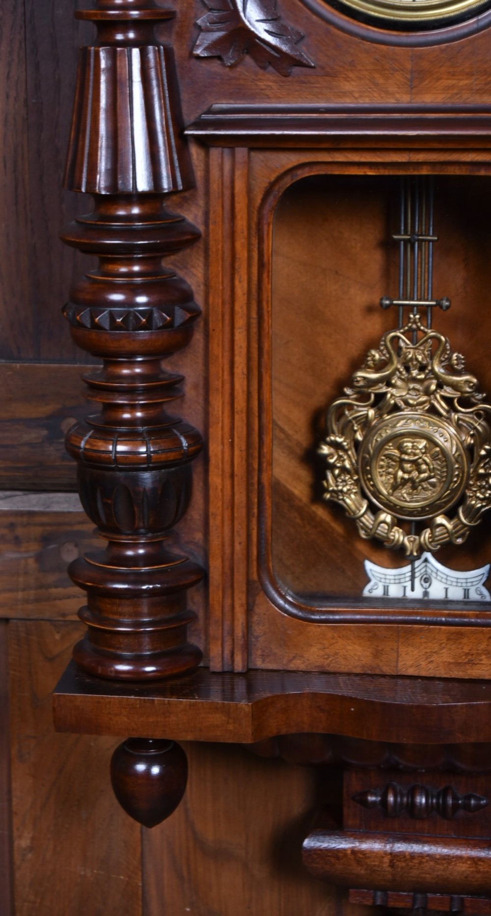 An antique dark walnut wall clock featuring a carved horse crest, turned side pilasters, and a decorative brass pendulum behind a glass door. View IX