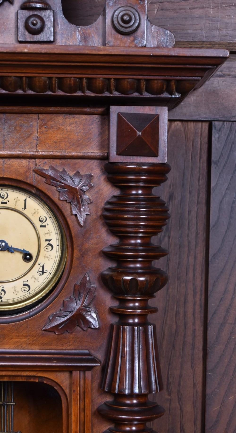 An antique dark walnut wall clock featuring a carved horse crest, turned side pilasters, and a decorative brass pendulum behind a glass door. View XI