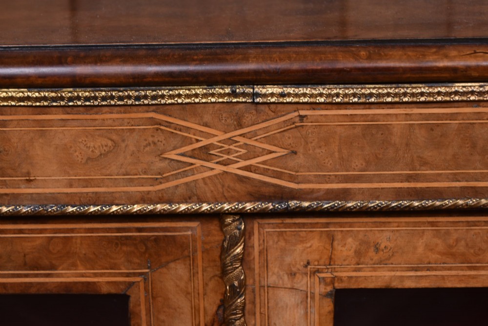 A Victorian burr walnut low cabinet featuring two glazed doors, intricate boxwood inlay, and ornate bronzed corner mounts. View V