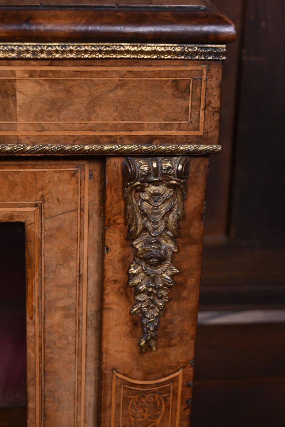 A Victorian burr walnut low cabinet featuring two glazed doors, intricate boxwood inlay, and ornate bronzed corner mounts. View VI